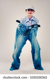 Caucasian Boy Wearing His Dad's Shirt, Jeans And Tie On Light Background. He Is Wearing Big Adult Size Clothes Which Are Too Big For Him.