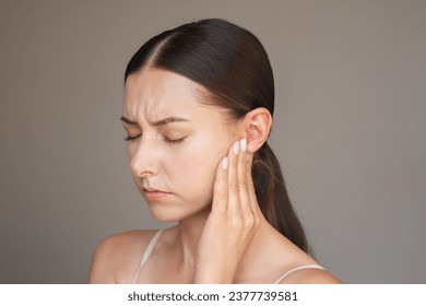 Caucasian brunette woman is experiencing acute pain in her ear. She frowns, closes her eyes, presses her ear with her fingers. Suffers from otitis. - Shutterstock ID 2377739581