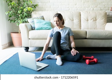 Caucasian Brunette Woman Looking At An Online Workout Routine On Her Laptop Computer While Exercising At Home