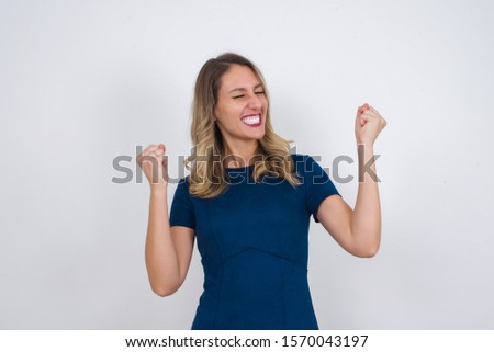 Caucasian brunette woman rejoicing her success and victory clenching her fists with joy. Lucky woman being happy to achieve her aim and goals. Positive emotions, feelings.