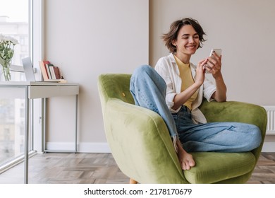 Caucasian brunette woman smiling at phone . Full view of pretty young woman holding and chatting on smartphone in home. Technology, lifestyle  - Powered by Shutterstock