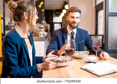 Caucasian business couple dressed strictly in the suits having discussion sitting together at the restaurant during the dinner