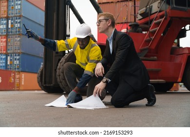 Caucasian Business Man And Black Foreman In Yellow Safety Jacket Kneed On The Floor While Discussing Together At Container Yard Outdoor.