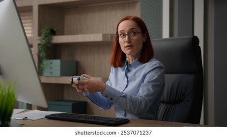 Caucasian business woman office worker at workplace break pause work addicted video game playing console controller businesswoman play online while nobody see girl get caught pretend working smiling - Powered by Shutterstock