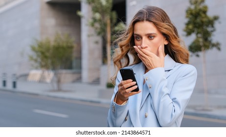 Caucasian business woman outdoors hold mobile phone read unpleasant sms awful news feel indignant covers mouth shocked face. Bad notice from bank blocked account broken smartphone shock astonishment