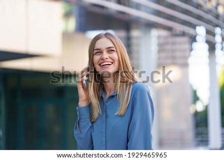 Caucasian business woman speaking by phone. Waist up portrait of a successful European woman, talking on the phone, standing on glass background, modern office building.