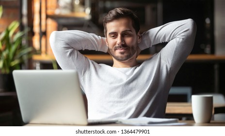 Caucasian businessman sitting at table in cafe modern cozy office looking at laptop screen feels satisfied proud with done work, serene man resting putting hands behind head relaxing no stress concept