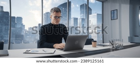 Caucasian Businessman Standing In Corner Office And Holding Laptop Infront Big Window With Megapolis Cityview. Professional CEO Sitting Down At Desk And Starts Typing On Computer.