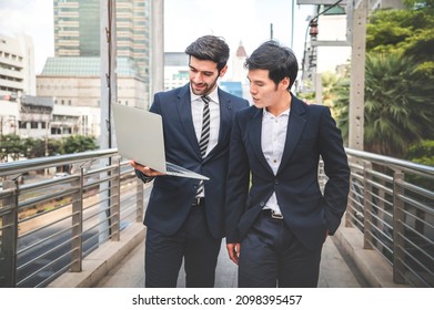 Caucasian businessman walking and talking to Asia businessman colleague by use laptop while leaving office building during lunch break. - Powered by Shutterstock