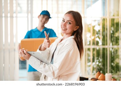 Caucasian businesswoman checklist online order best seller product and thumbs up about professional delivery while Asian worker man holding cardboard for shipping