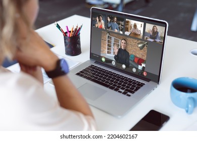 Caucasian businesswoman at desk making laptop video call with diverse colleagues waving. Business communication, working remotely and digital interface concept. - Shutterstock ID 2204602167