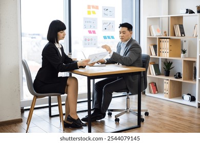 Caucasian businesswoman presents report to Asian businessman in modern office setting. Professional attire and focused expressions indicate important discussion and decision-making process. - Powered by Shutterstock