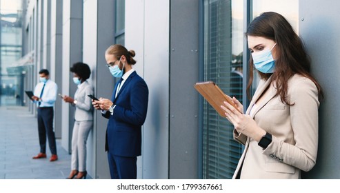 Caucasian Businesswoman Using Tablet Device At Street. Line Of Mixed-races Business People In Medical Masks Standing Outdoors And Keeping Social Distance. Coronavirus Concept. Pandemic. Multiethnic.