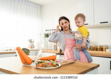 Caucasian Busy Mother Doing Housework With Baby Boy Toddler In Kitchen. Beautiful Single Mom Use Phone Call For Work And Cook Foods Prepare Breakfast For Little Kid Son In House. Family-housekeeping.