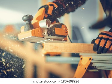 Caucasian Carpenter With Corded Wood Planer In His Hand Planing Wood Plank. Construction Site Theme.