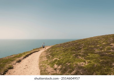 Caucasian casual attire man walking Whippet dog along clifftop coastal path towards Bedruthan Steps with stunning sea views and green hills on a sunny day, overlooking the sea Cornwall, UK - Powered by Shutterstock