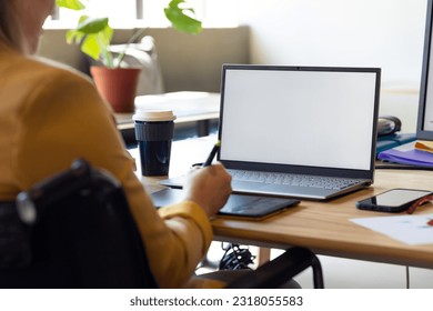 Caucasian casual businesswoman in wheelchair using graphics tablet and laptop, copy space on screen. Casual office, disability, inclusivity, communication, business and creative work. - Powered by Shutterstock