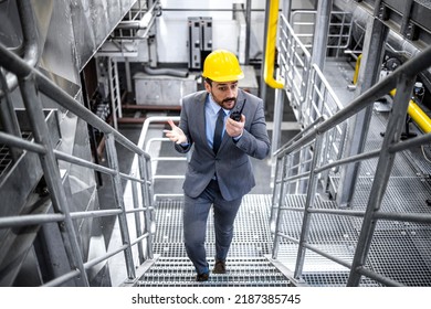 Caucasian CEO or factory manager in suit and yellow hardhat walking through plant checking production. - Shutterstock ID 2187385745