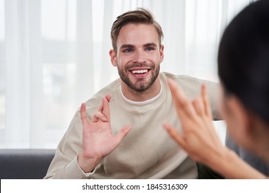 Caucasian Cheerful Man And Dark Haired Woman Communicating With Pleasure Emotions With Sign Language While Sitting The Sofa. Husband And Wife Confessing Their Love To Each Other In The Language Of The