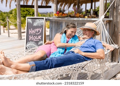 Caucasian cheerful senior couple lying on hammock at beach outside restaurant. Unaltered, retirement, vacation, tourist resort, love, together, lifestyle, relaxation and enjoyment concept. - Powered by Shutterstock