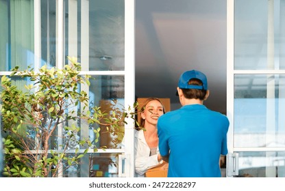 Caucasian cheerful woman happily receives a package from a delivery man in a blue uniform with cap at her door showcasing positive customer and fast service - Powered by Shutterstock