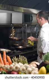 Caucasian Chef In A Smoky Restaurant Kitchen Stirring Mushrooms By Flipping Them Into The Air.