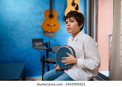 Caucasian child boy musician playing drums, creating rhythm of music, enjoying the ethnic African traditional culture. Teenage boy playing djembe in modern interior with different musical instruments - Powered by Shutterstock