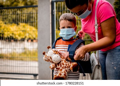 Caucasian Child Getting Ready To Go To Kindergarten In Pandemic Times, His Mom Is Helping Him To Wear Mask Before He Goes 