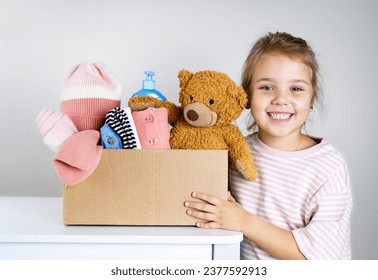 Caucasian child girl holding donation box with kid's stuff: clothes, toys, warm clothing. Donate concept. Little volunteer. - Shutterstock ID 2377592913