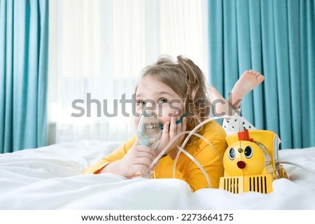 Caucasian child making inhalations laying in bed.. Kid girl using nebulizer. Health treatment.