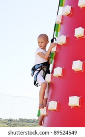 Caucasian Child Undergoin Treatment For Cancer Climbing A Blow Up Castle At A Fun Fair