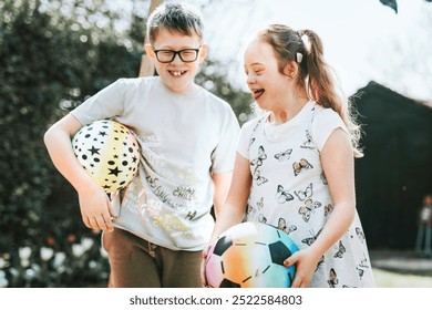 Caucasian children, boy and girl, playing with colorful balls. Siblings, boy and girl are smiling, enjoying their time outdoors with their colorful balls. Girl with Down Syndrome playing with sibling - Powered by Shutterstock