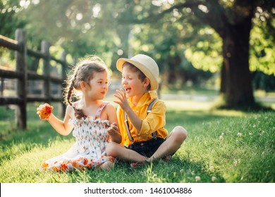 Caucasian children boy and girl siblings sitting together sharing apple. Two kids brother and sister eating sweet fruit in park on summer day. Best friends forever. Healthy happy childhood.