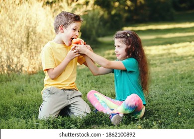 Caucasian Children Boy And Girl Siblings Sitting Together Sharing Apple. Two Kids Brother And Sister Eating Sweet Fruit In Park On Summer Day. Best Friends Forever. Healthy Happy Childhood.