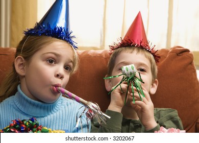 Caucasian children looking bored wearing party hats and blowing noisemakers. - Powered by Shutterstock