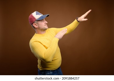 Caucasian Chubby Dancing Man In Casual Clothes Jeans, Jacket And Cap. Dances Pointing To The Side With His Hands