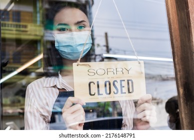 Caucasian coffee owner wear mask due pandemic, turns sorry closed sign. Attractive young girl waiter closed sign to shut down business due to financial crisis from COVID-19 lockdown and quarantine. - Shutterstock ID 2176148791