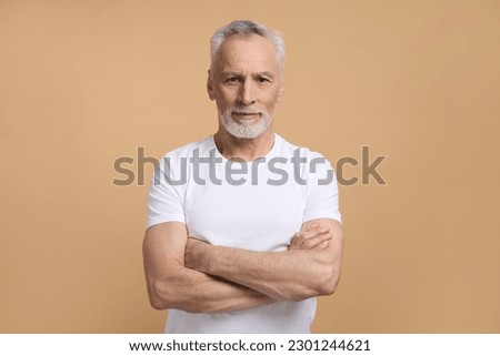 Caucasian confident handsome imposing retired senior man 60 years old, smiling, looking confidently at camera, posing with arms folded isolated on beige background. Mature people and lifestyle concept