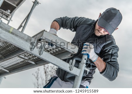 Caucasian Construction Worker Installing Scaffolding Elements. 