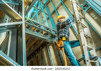 Caucasian Contractor Climbing A Ladder Inside Steel House Frame Construction During Its Development Work. New Commercial Unit Building.