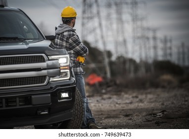 Caucasian Contractor Field Work Job. Worker and His Pickup Truck. Countryside Remote Location with High Voltage Poles in the Background.