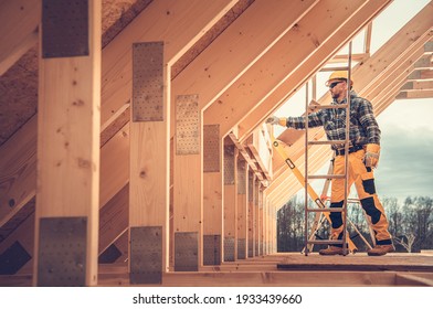 Caucasian Contractor In Hard Hat And His Residential Building Wooden Skeleton Construction Job. House Wood Frame.