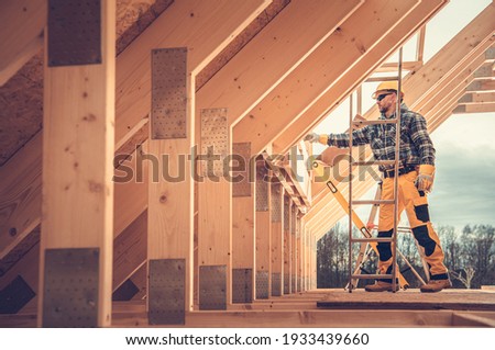 Caucasian Contractor in Hard Hat and His Residential Building Wooden Skeleton Construction Job. House Wood Frame.