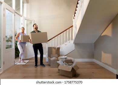 Caucasian Couple Arriving At Their New Home Walking Through The Front Door And Standing In The Hallway Carrying Cardboard Packing Boxes And Looking Around Smiling, Open Packing Boxes On The Floor