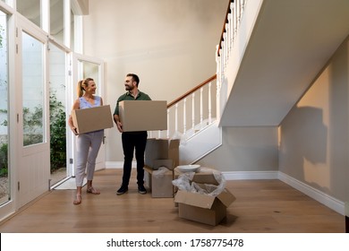 Caucasian Couple Arriving At Their New Home Walking Through The Front Door And Standing In The Hallway Carrying Cardboard Packing Boxes And Smiling, Open Packing Boxes On The Floor Beside Them