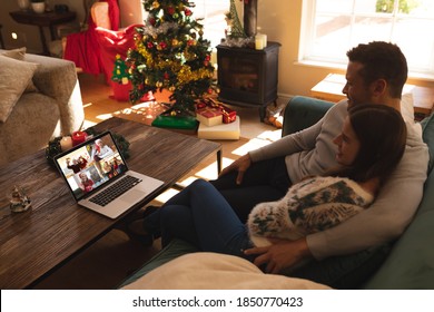 Caucasian Couple At Christmas, Sitting On Sofa At Home Embracing Having Video Chat With Friends And Family On Laptop Screen. Social Distancing During Covid 19 Pandemic At Christmas Time.