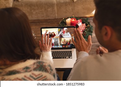 Caucasian Couple At Christmas, Sitting On Sofa At Home Having Video Chat With Friends And Family On Laptop Screen, Waving. Social Distancing During Covid 19 Pandemic At Christmas Time.