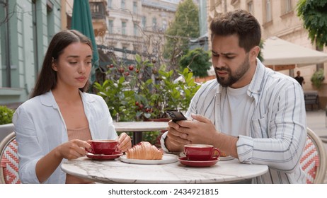 Caucasian couple eat breakfast in city cafe outdoors addicted busy man boyfriend using mobile phone ignoring upset woman girlfriend offended arms crossed quarrel crisis relationship problem conflict - Powered by Shutterstock