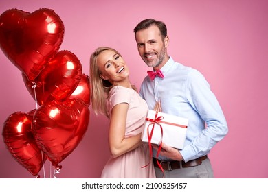 Caucasian couple holding a bunch of red balloons and a gift box