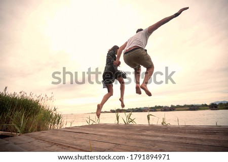 caucasian couple jumping together in the river holding hands